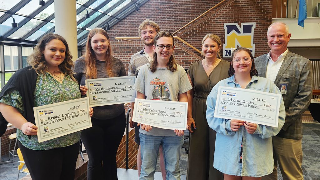 Four high school age students holding award checks standing with three adults in an awards ceremony