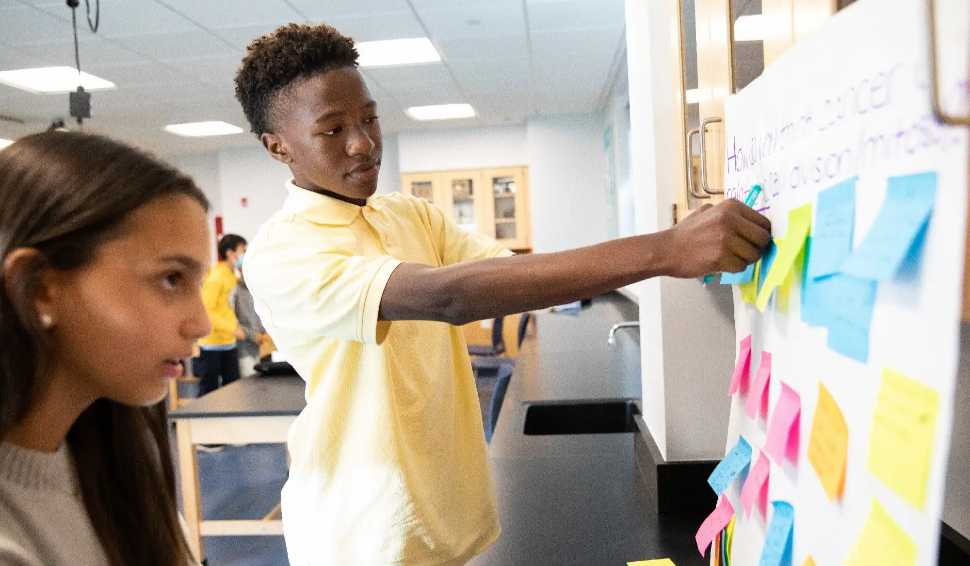 Students adding sticky notes to a whiteboard during a brainstorming activity.