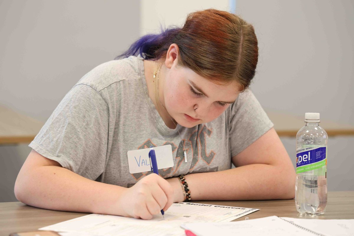 A female middle school student concentrating intently while writing on a piece of paper.