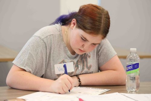A female middle school student concentrating intently while writing on a piece of paper.