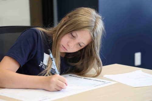 A female middle school student concentrating intently while writing on a piece of paper.